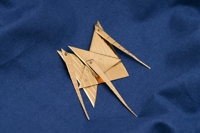 Abstract gold-coloured metal jewellery piece designed by Qona Rankin. Multiple triangle shapes are joined together to create a small brooch. 