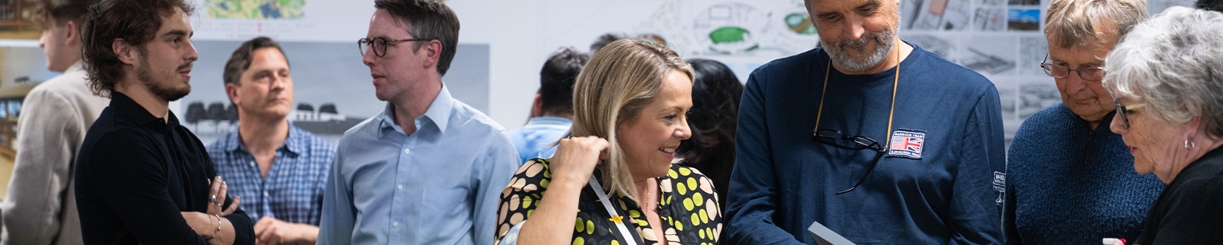 Photograph of a group of creative academics and professional staff talking to each other and gesturing towards various models and books at a networking event.