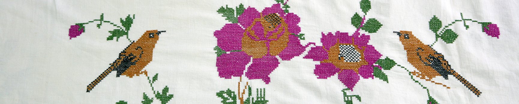 Embroidery of two open pink flowers with buds and two light brown birds on a white fabric.